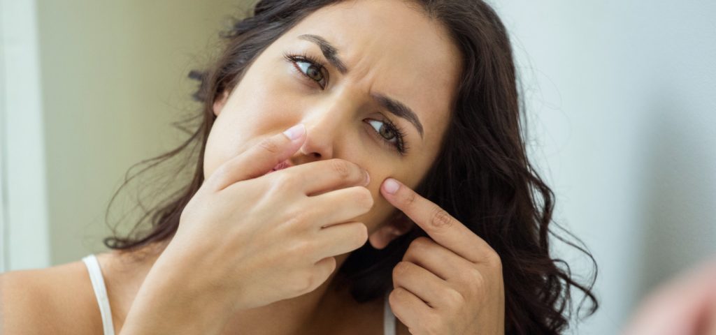 Adult woman looking at acne in the mirror